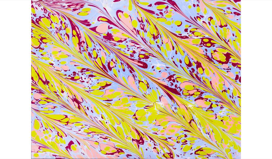 Colourful paper marbling design with swirling pink, yellow and purple patterns created in a paper marbling workshop.