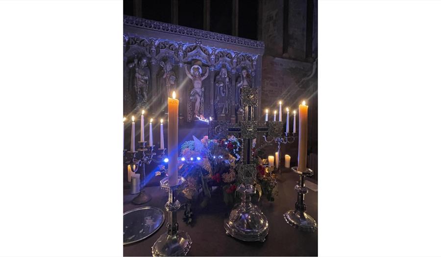 Image shows the Altar at St Thomas the Martyr Church with tall candles that are alight and an image of Jesus in the background on the cross.