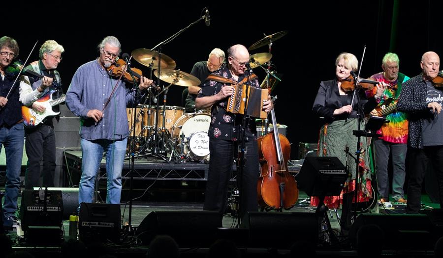 Photo of folk musicians on stage with string instruments.