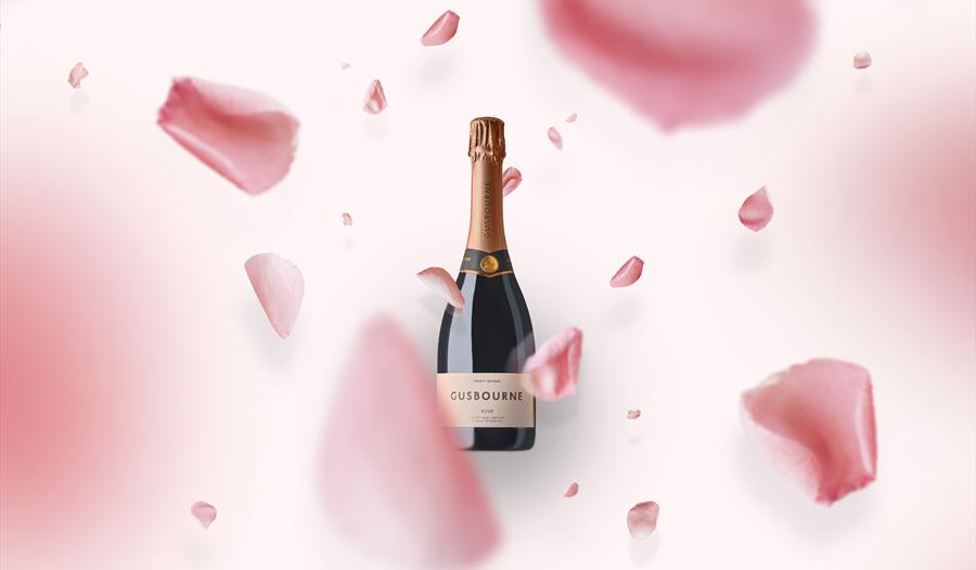 a bottle of gusbourne wine on a pink background with falling flower petals