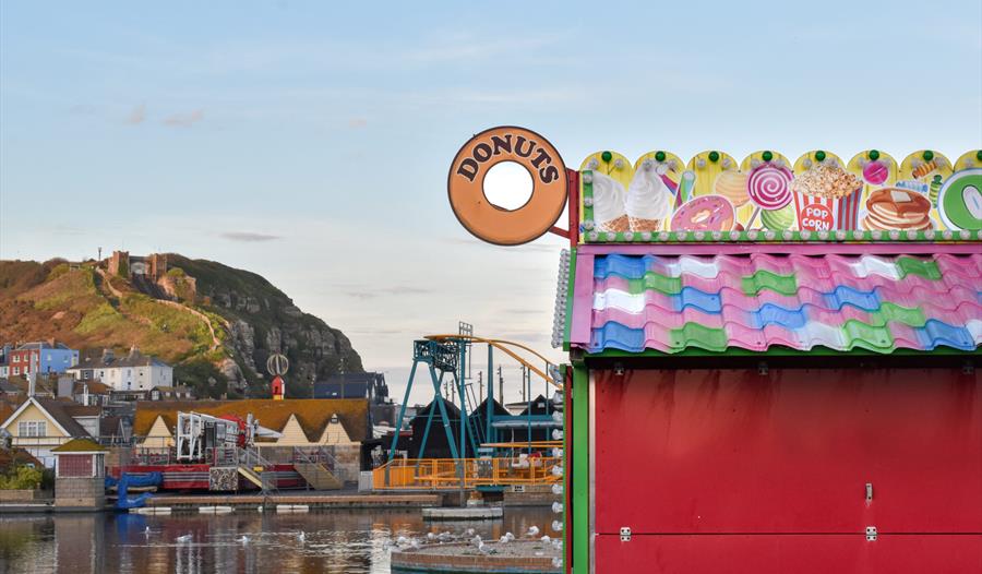 photograph of Hastings, with donut sign and colourful hut in the foreground and hill with funicular railway in the background.