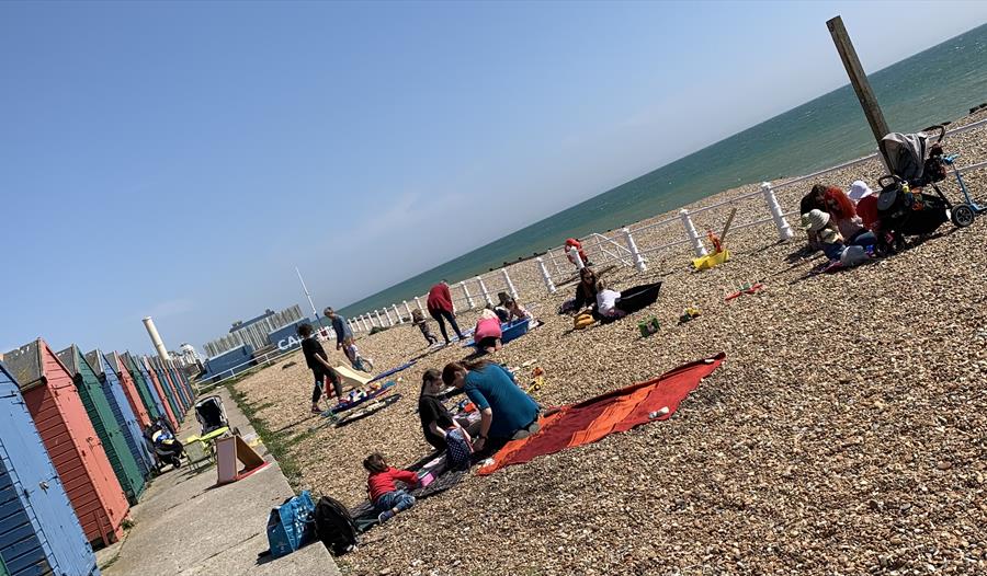 pebble beach with beach huts and people sitting on picnic blankets