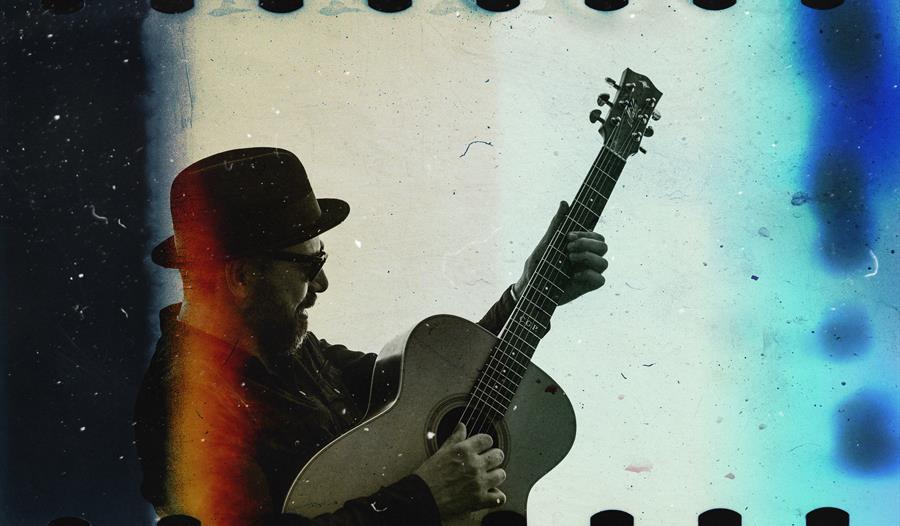 35mm film image with visible sprocket holes. Shows a man in a bowler hat playing guitar.