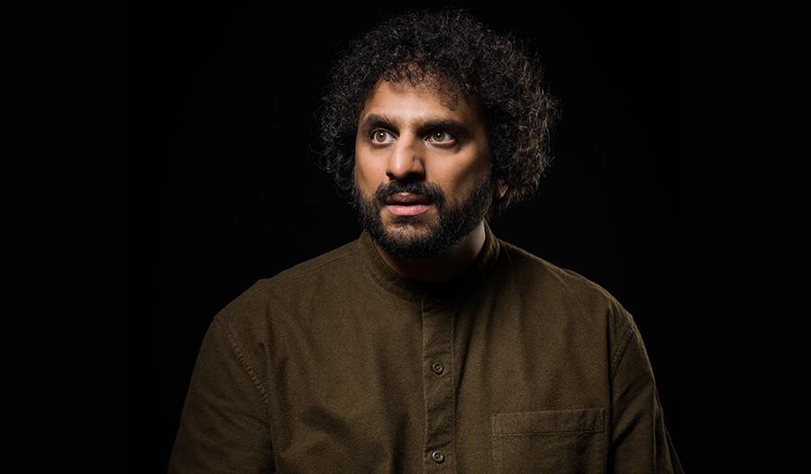 Nish Kumar on a black background wearing brown