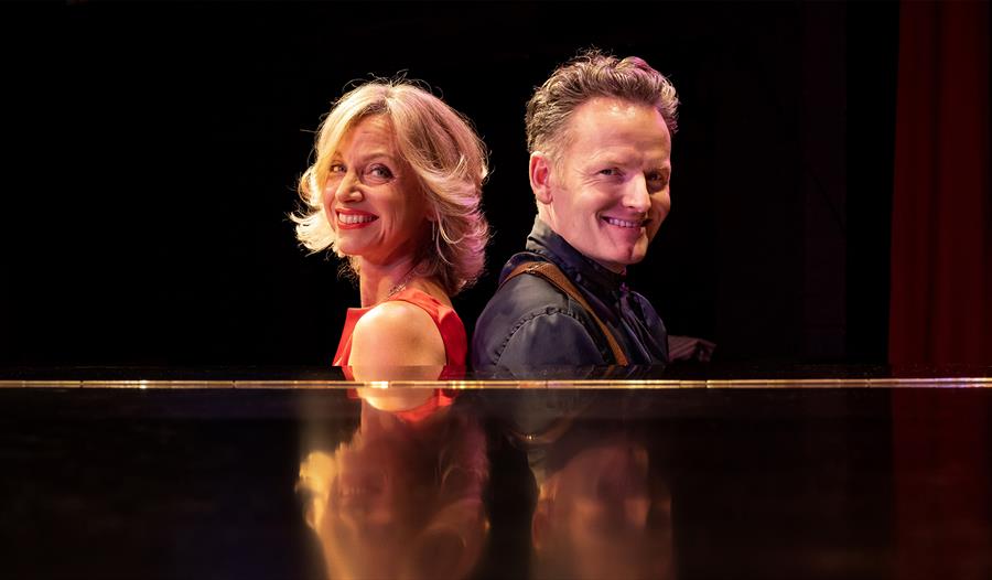 Photograph of Liza Pulman and Joe Stilgoe sat by a piano.