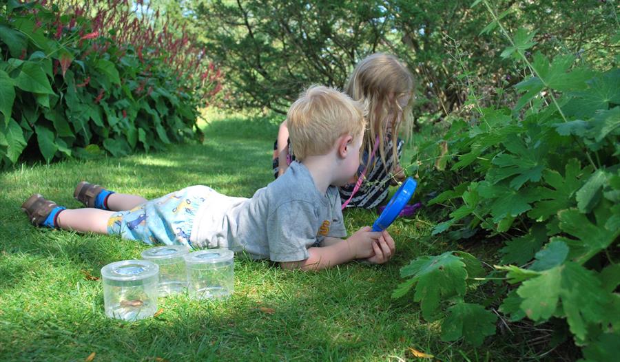 two young children exploring in a garden with pots and a magnifying glass.