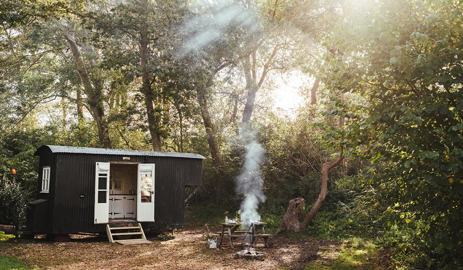 Photograph of a black glamping hut in a woods with smoking fire.