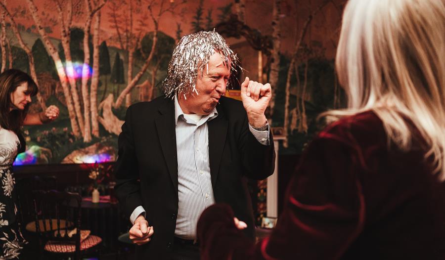 man with foil silver wig making shapes on the dancefloor.