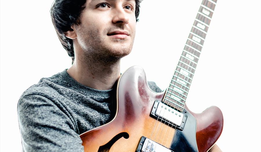 white man with dark hair hugging his guitar, white background