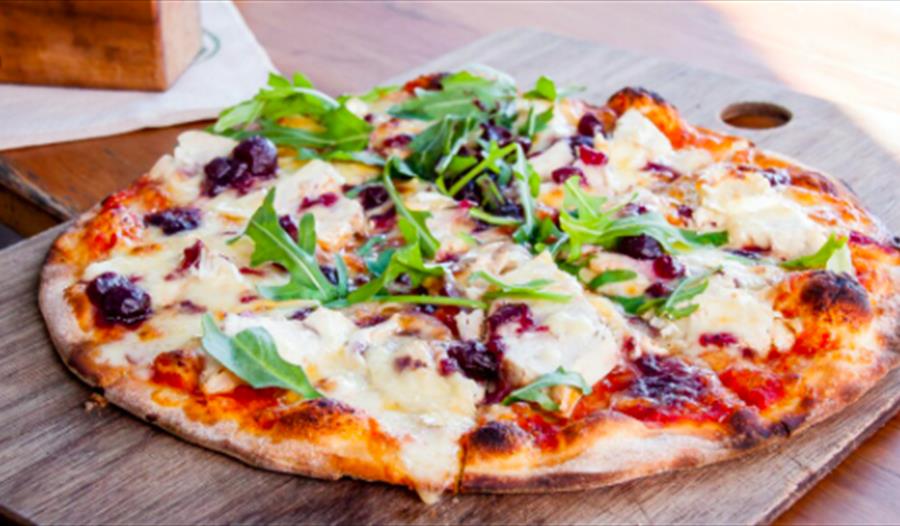 A photograph of a pizza topped with mozzarella and rocket, placed on a chopping board. For a pizza night event at the hub bodiam rother
