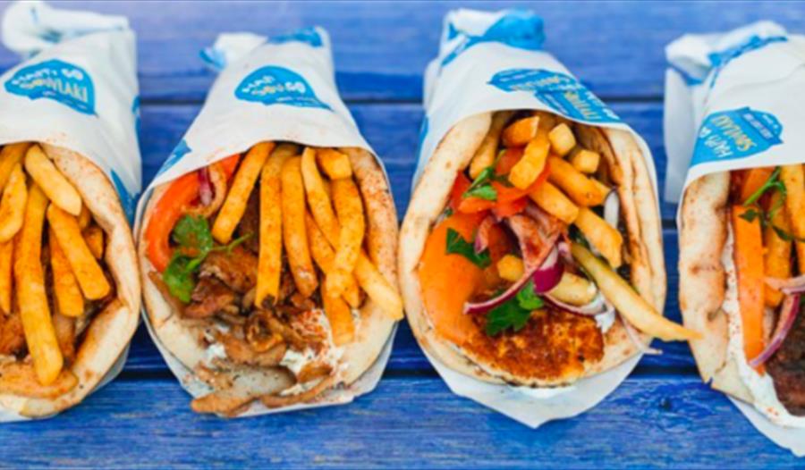 A photograph of four wrapped soulakis in a row, on a blue bench table. Photo for food event at the hub bodiam rother