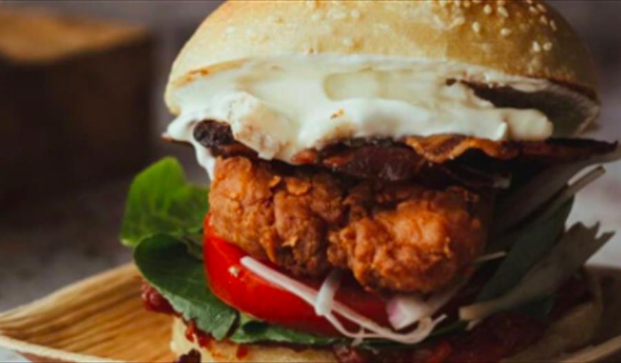 A close up of a stacked burger in a seeded bun, on a bamboo plate. To advertise The Pork Box event at The Hub, Bodiam, Rother.
