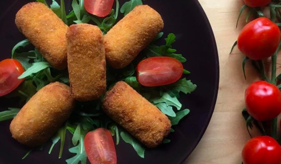 Tapas food, fried food arranged on a black plate with rocket leaves and tomatoes. For an event at The Hub, Bodiam, Rother.