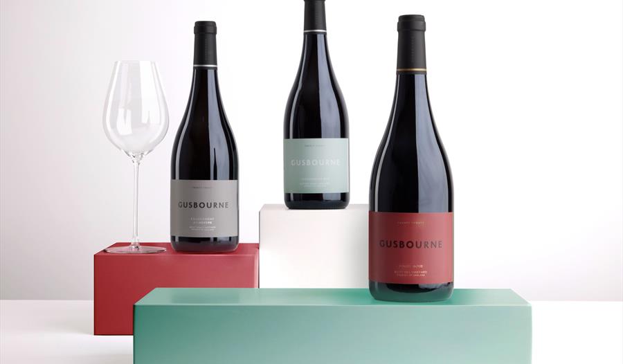 three wines bottles staggered on green, white and red box stands, against white background.