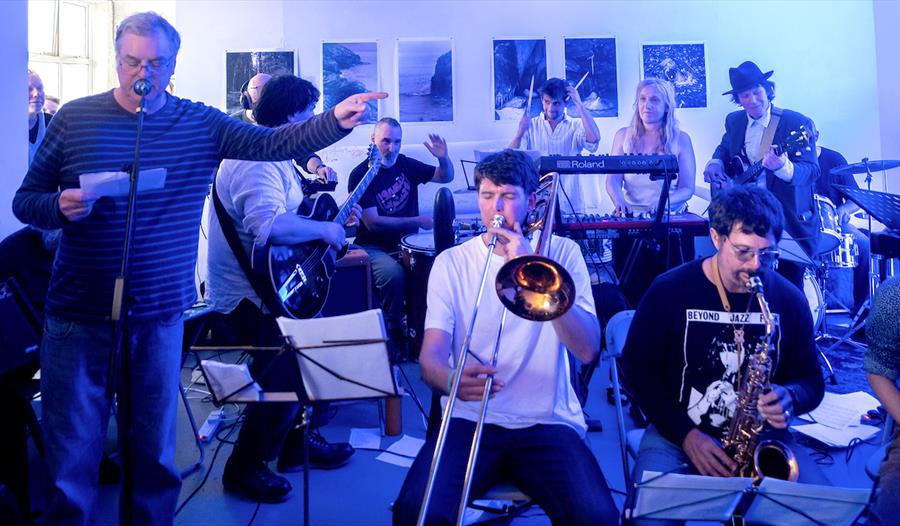 Live benefit concert featuring a large ensemble with brass, guitars and keyboards performing indoors for the Refugee Buddy Project.