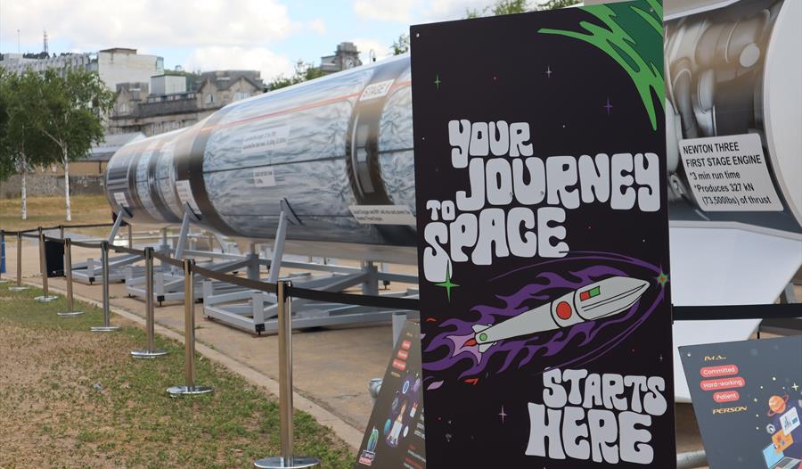 picture of a large replica rocket mounted for display outdoors. A display panel in the foreground says 'Your journey to space starts here'.