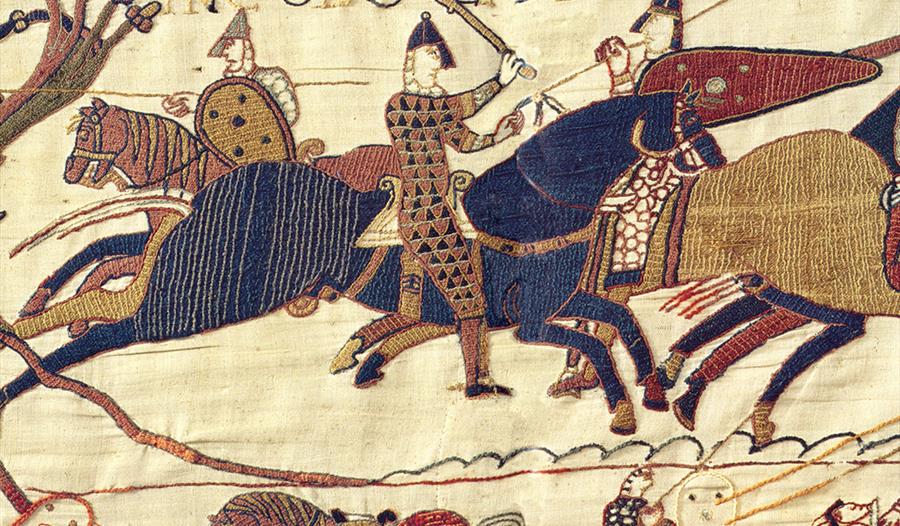 a section of the Bayeux tapestry, medieval embroidery shoes stitched image of a knight with helmets and swords on horseback.