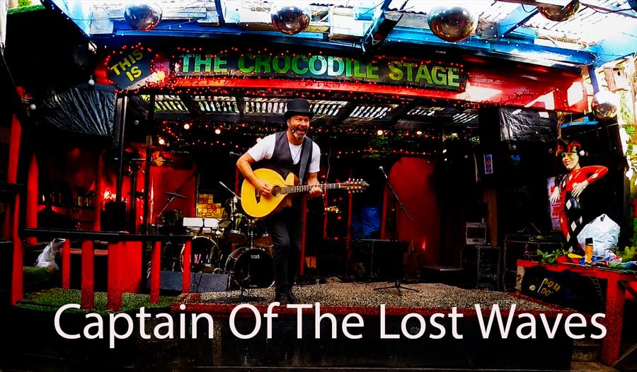 Musician playing guitar on the Crocodile Stage, promoting a Captain Of The Lost Waves live performance.
