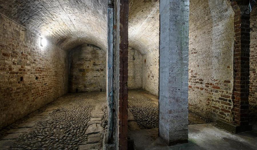 Brick-vaulted underground rooms of the buried Swan Hotel Coach House in Hastings, with stone pillars and cobbled floors.