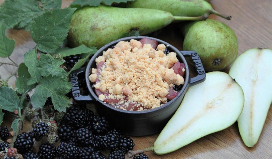 Photograph of small crumble dish with pears and berries surrounding.