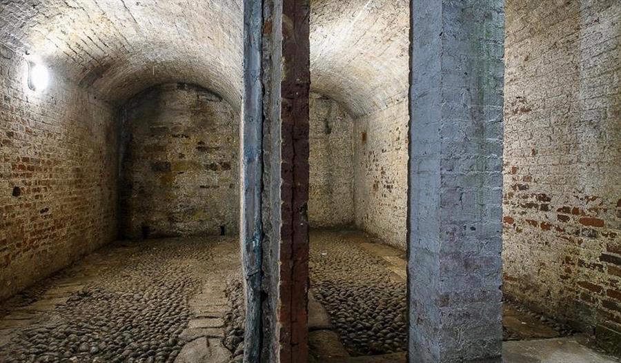 Historic brick coach house interior with vaulted ceilings, cobbled floor and stone pillars, open to visitors.