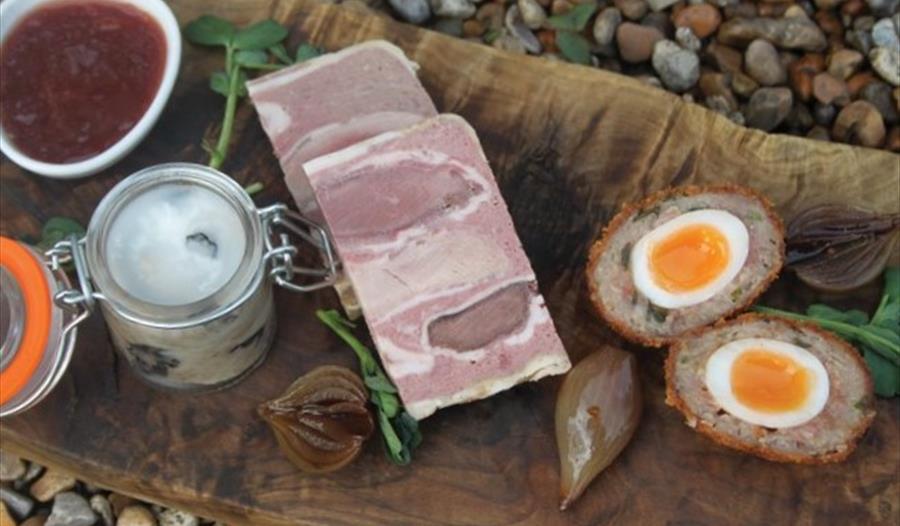gourmet ham and a scotch egg served on a wooden platter.