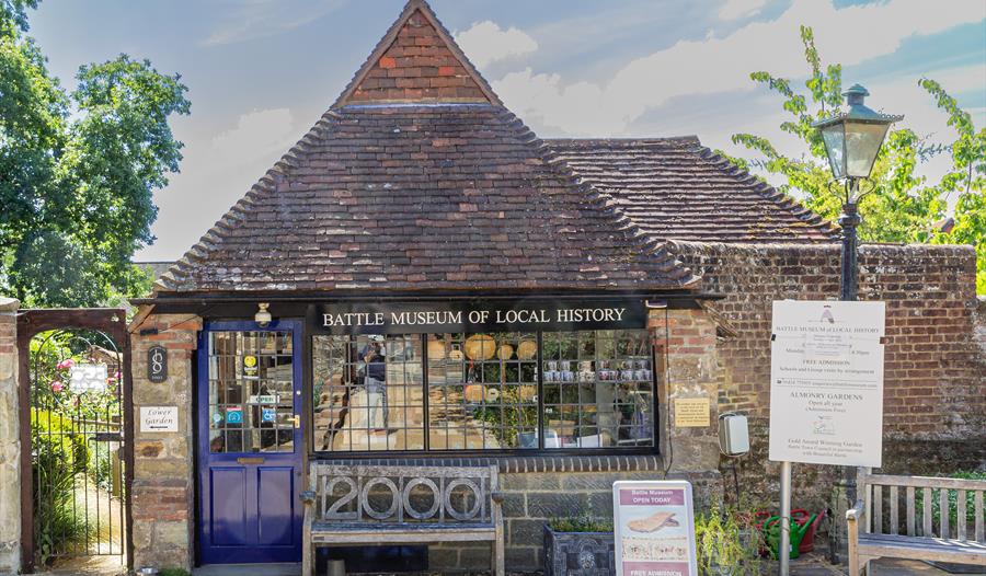 front external view of battle museum. A small brick building with pointed tiled roof with a weathervane on top.