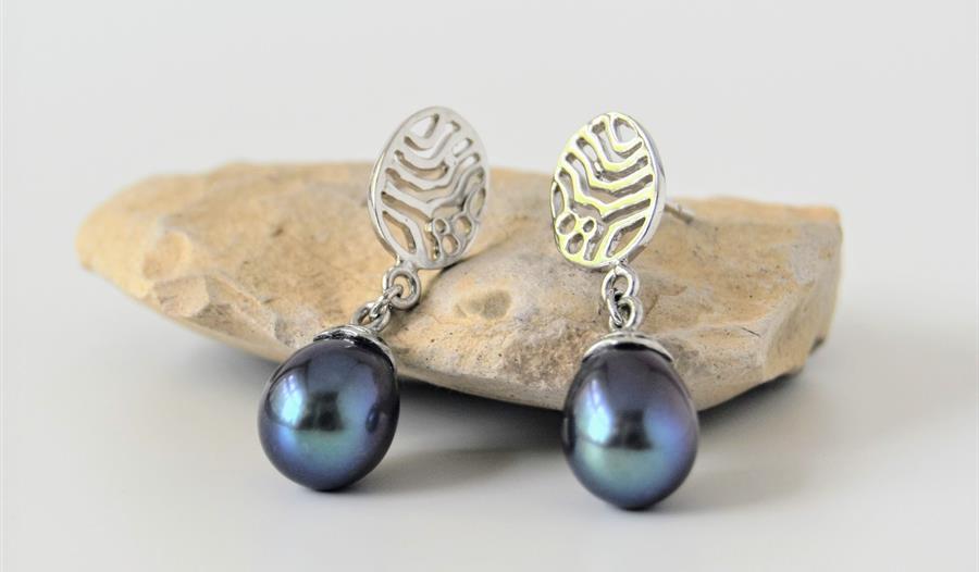 a photograph of earings placed on a small light coloured stone. Silver dangling earings with blue pearlescent stone.