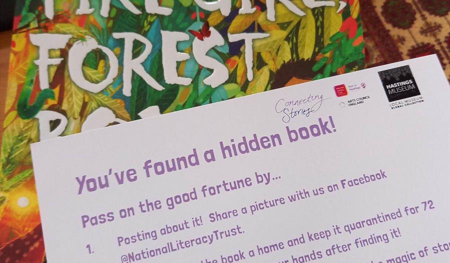 A photograph of a book with a postcard on top. Postcard says 'You've found a hidden book!'. To promote event at Hastings Museum.
