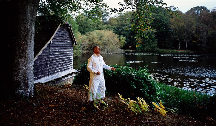 Photographic artwork showing a figure by a lakeside woodland and boathouse, featured in PhotoHastings Festival.