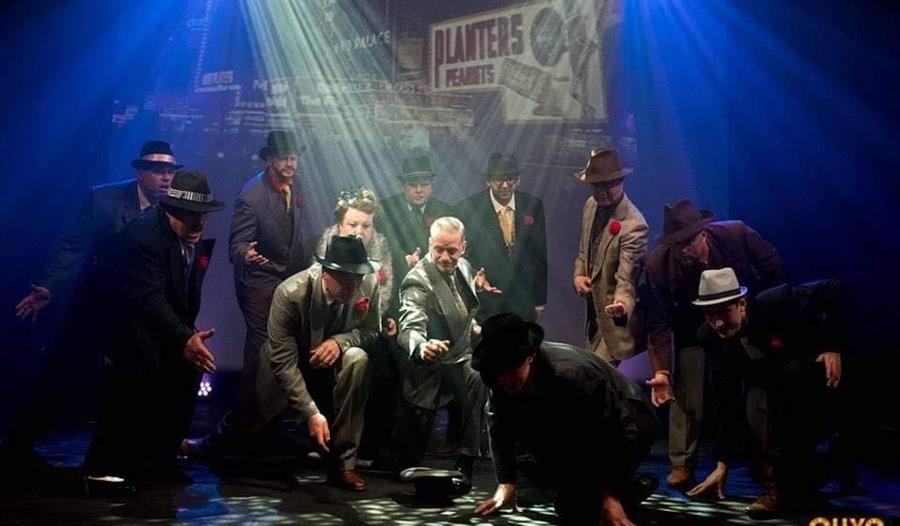 A group of men dancing on stage wearing suits and trilby hats.