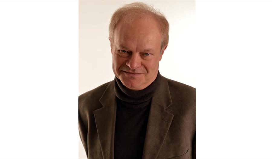 a photograph of a white man wearing black roll neck sweater and blazer.