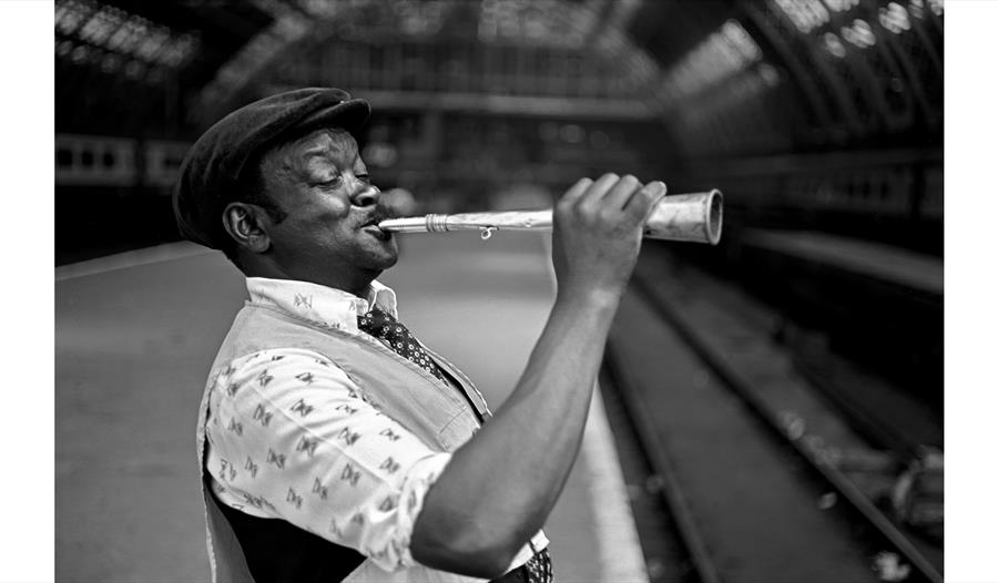 photograph by bob mazzer man on train platform blowing a horn instrument
