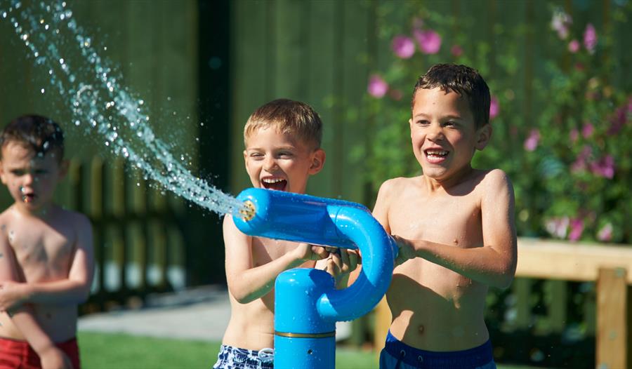 Three young boys dressed in swimming trunks, playing with a fun water sprinkler.