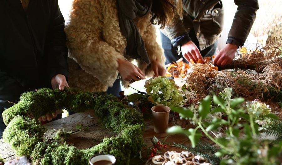 close of workbench with hands busy preparing christmas wreaths with moss and foliage.