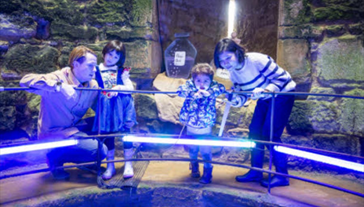 image shows a group of 2 adults and 2 children in Bodiam Castle looking at something off screen.