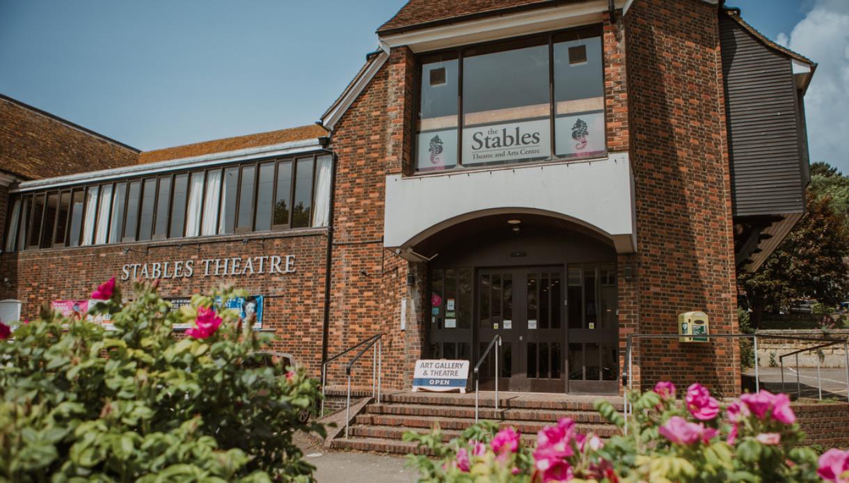 Exterior of The Stables Theatre, Hastings, a brick-built arts venue framed by colourful flower beds.