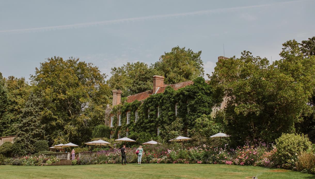 Pashley Manor house framed by flower-filled borders, lawns and mature trees in the gardens.