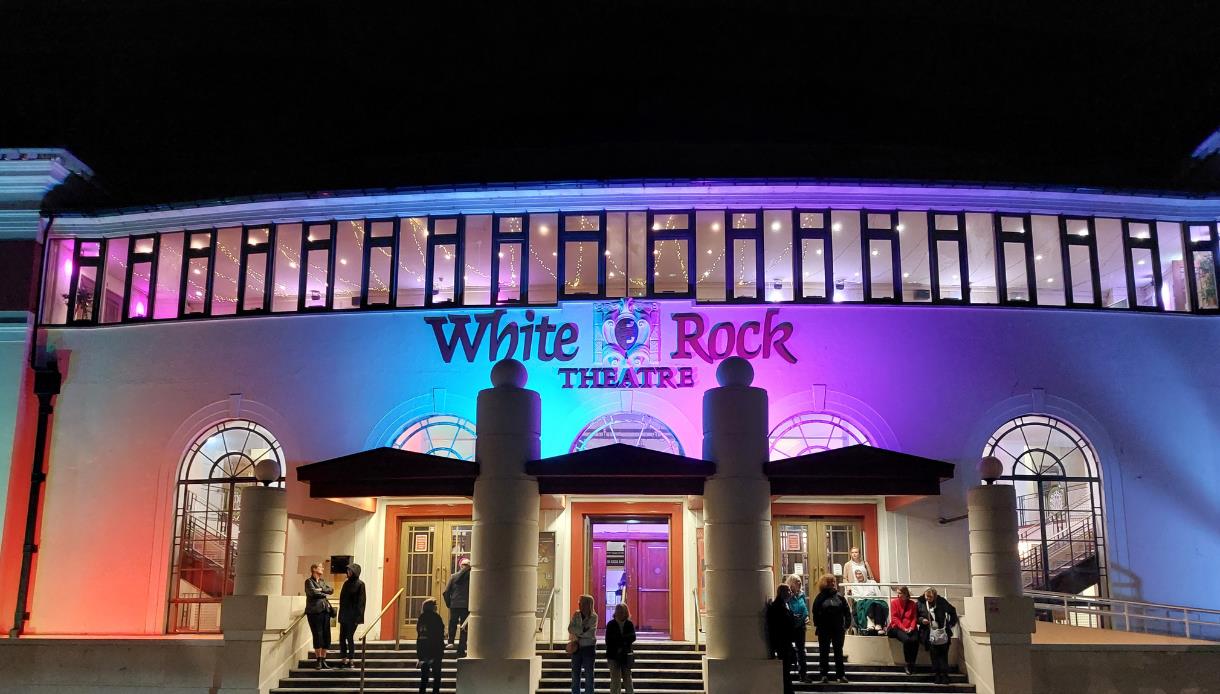 White Rock Theatre exterior lit at night with colourful lights and visitors gathered outside entrance.