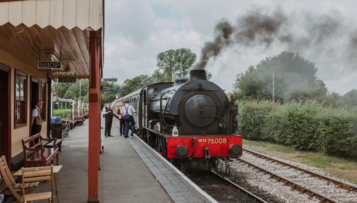Steam locomotive WD75008 at a Kent & East Sussex Railway station platform, with smoke rising overhead.