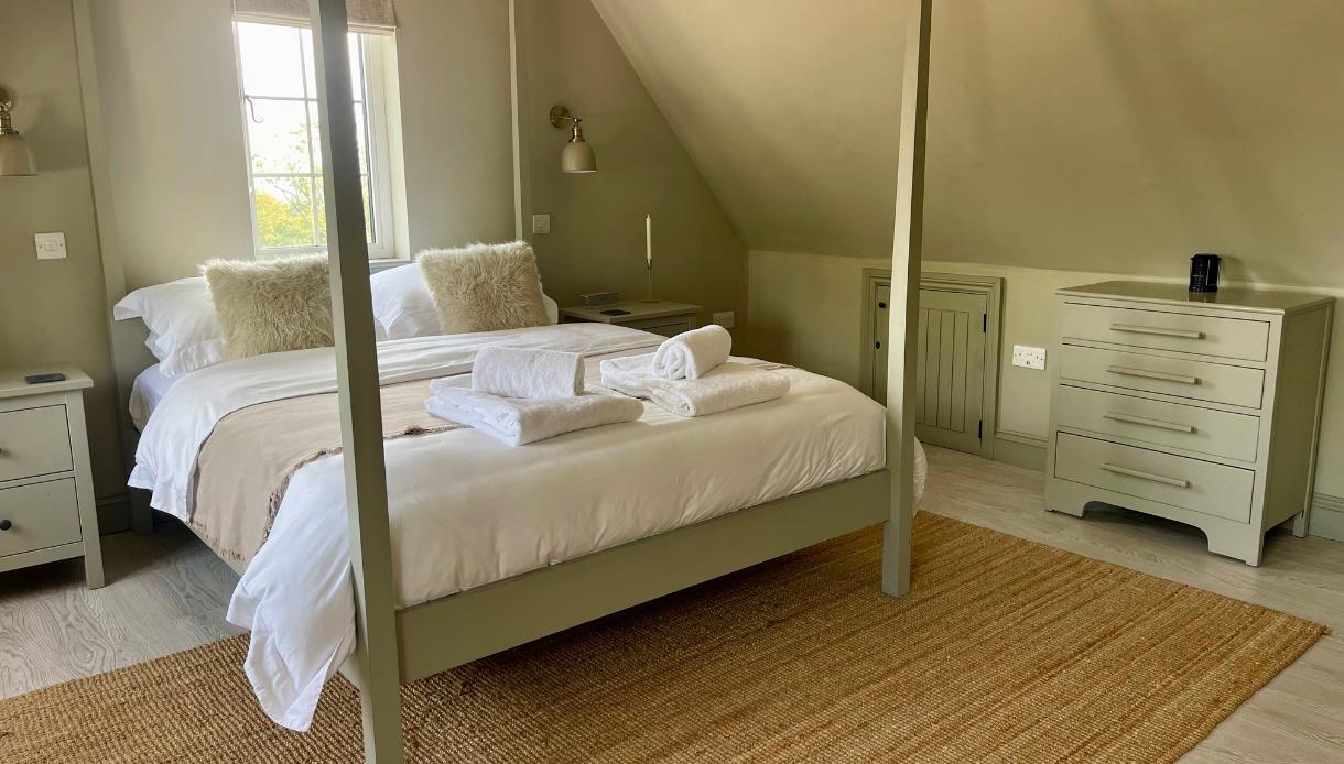 Spacious king bedroom at Judins Cottage, Burwash, with four-poster bed, soft furnishings and countryside views.