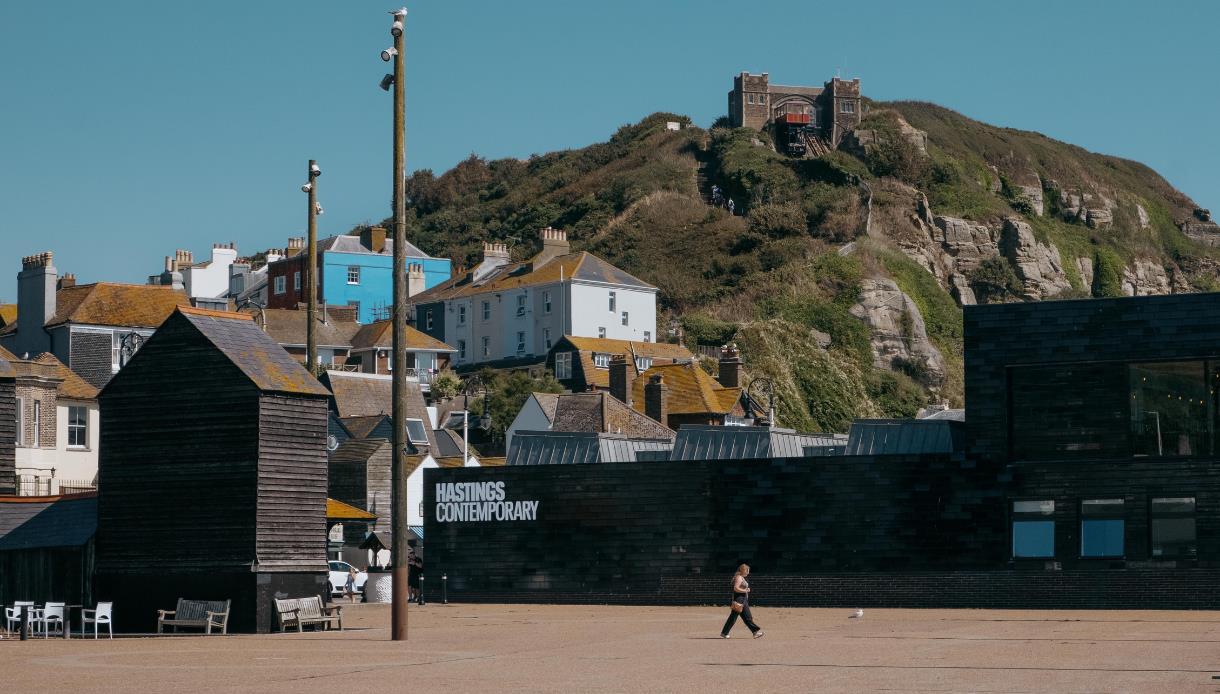 Hastings Contemporary gallery beneath East Hill cliffs, with Old Town buildings and fishing huts nearby.
