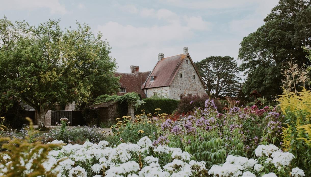 Michelham Priory surrounded by colourful flower beds and mature trees in the historic gardens.