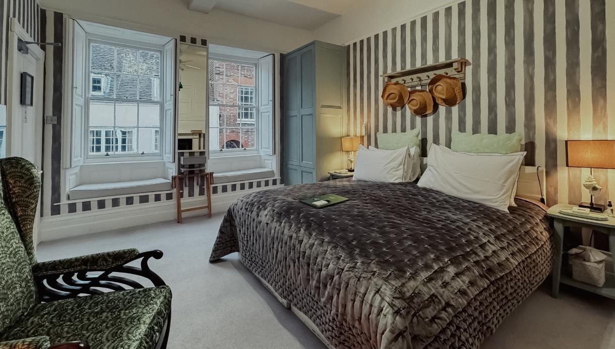 Stylish bedroom at The Laindons with striped wallpaper, bay windows, armchair and mirrored wardrobe.