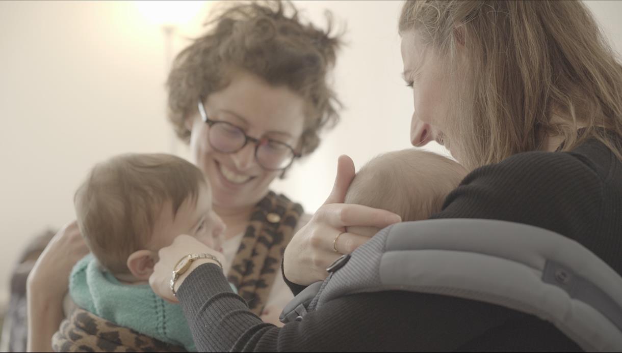 VoxSling event at The Crown Hastings: adults with babies sharing a warm, close moment in a softly lit indoor setting.