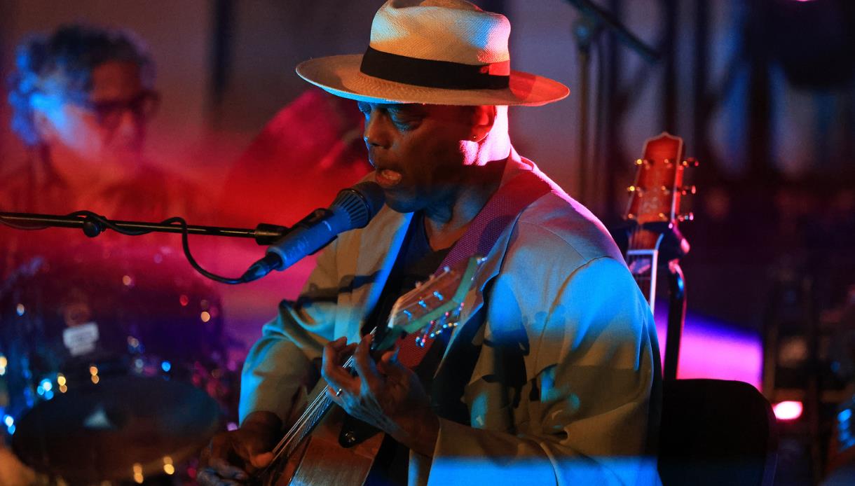 Live jazz performer singing and playing guitar under colourful stage lighting at Rye Jazz Festival.