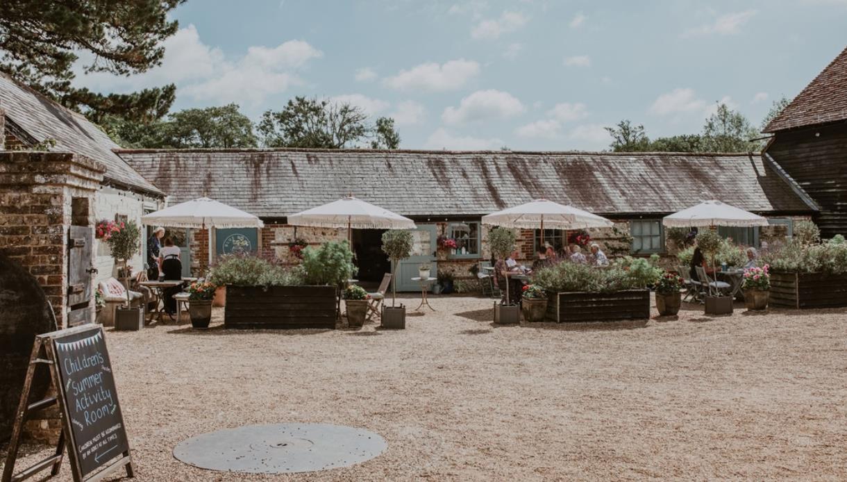 Michelham Priory courtyard café with outdoor seating, historic buildings and flower-filled planters.