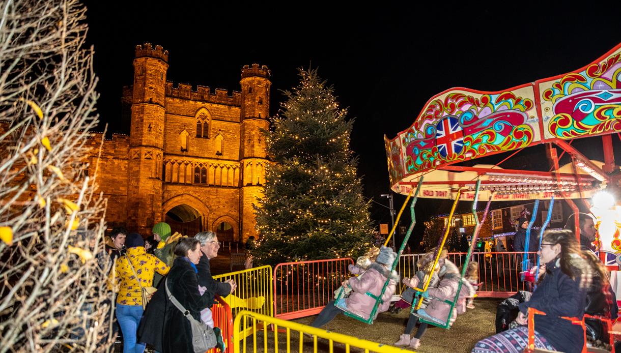 Nightime scene of children's carousel with Battle Abbey illuminated in the background.