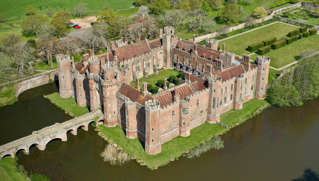 Aerial view of Herstmonceux Castle surrounded by a moat, gardens, and green parkland.