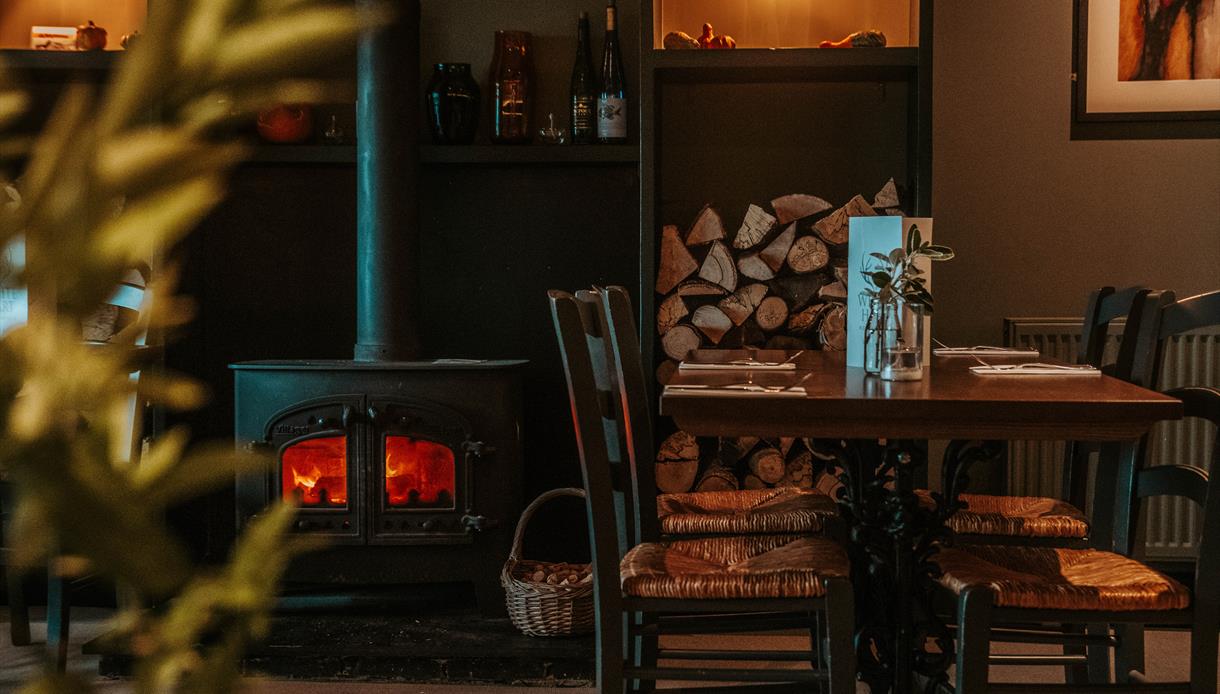 cosy pub interior with table and chairs next to a log burning stove.